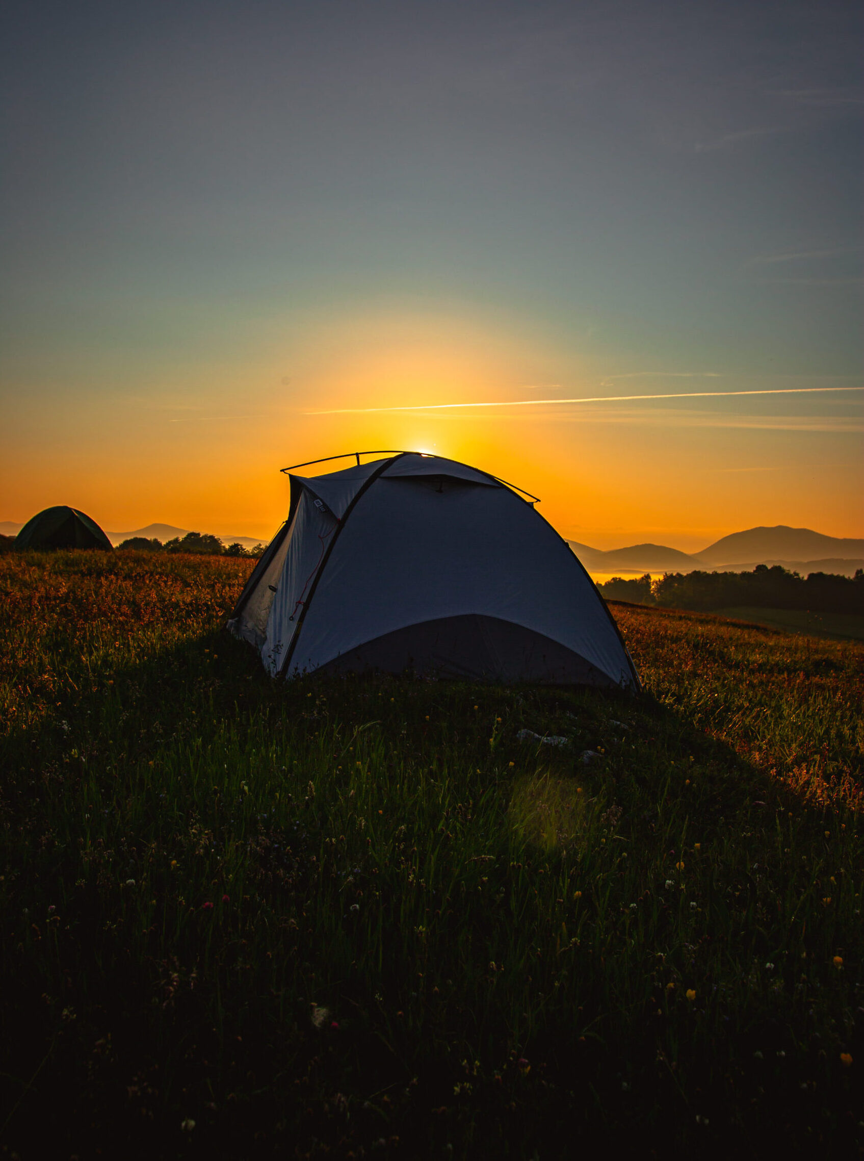 A vertical shot of a tent on a hill covered in greenery during a beautiful sunrise in the morning